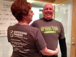 two volunteers show off the front and back of a GTG t-shirt promoting the values of a co-op during the owner loan campaign