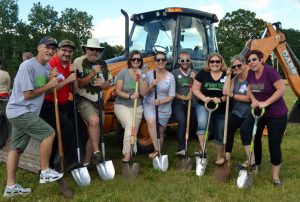 GTG Board members in a line with shovels in the ground, in front of a backhoe