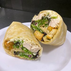 sliced wrap on white plate. Filled with chicken chunks, romaine lettuce, red onion, croutons, spinach, parmesan