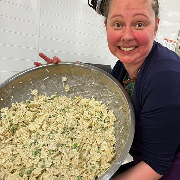 deli team member Liz holding a huge stainless steel bowl of pasta salad