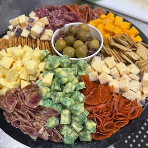 platter piled with a variety of cubed cheeses and sliced meats, with a bowl of olives in the center