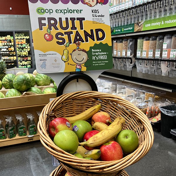 front of an in-store display in the aisles of Green Top Grocery. Baskets on the display hold a variety of apples, bananas, oranges