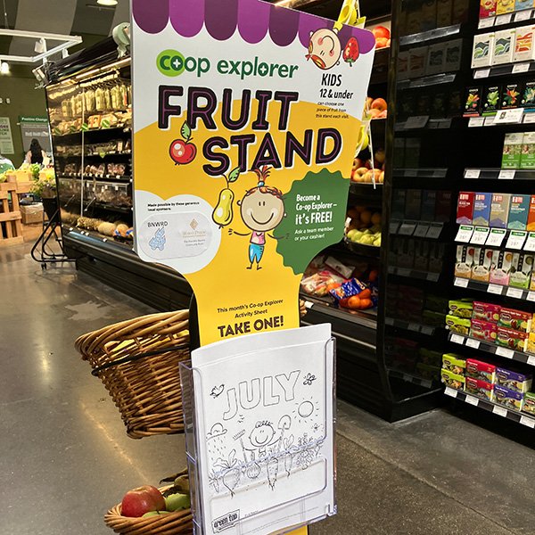 in-store display in the aisles of Green Top Grocery, with a bright yellow header sign saying 'Fruit Stand' with cartoons of kids and fruit.