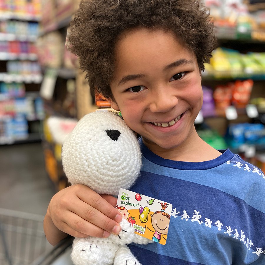 young Black boy smiling at the camera, holding a stuffed animal and a co-op explorer card.