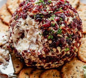 cheese ball covered in dried cranberries, pecans, and green herbs. Sitting on a platter surrounded by crackers