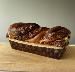 loaf of fresh baked chocolate nut babka in a paper pan